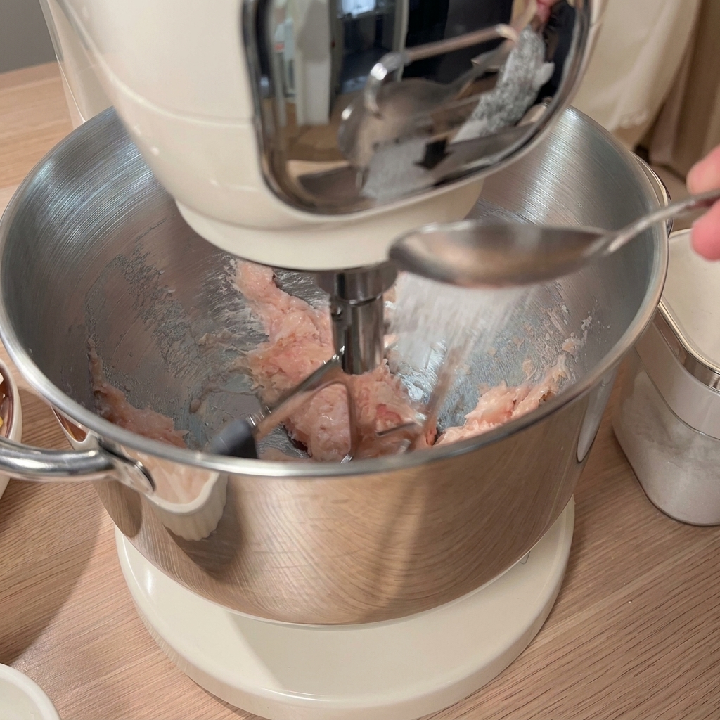 Une cuillerée dassaisonnement ajoutée au poulet haché dans le robot avec dautres ingrédients sur la table.