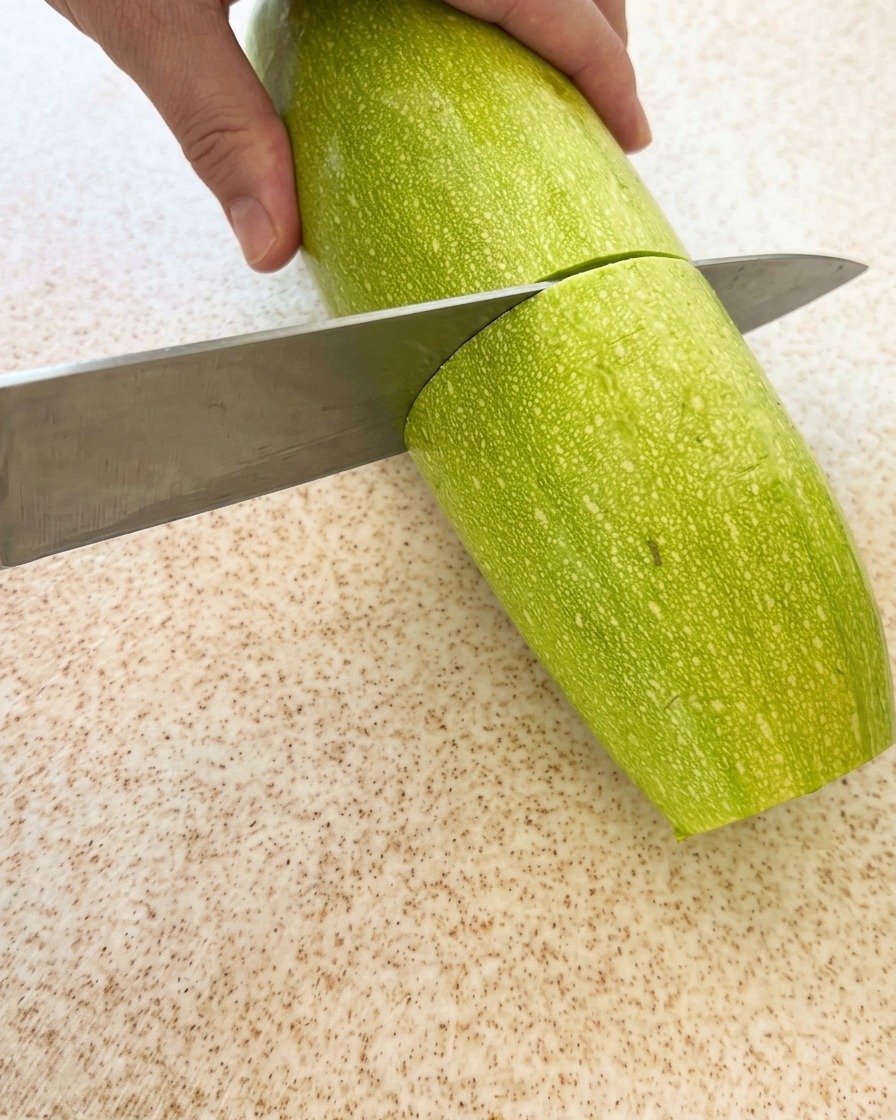 Une courgette verte fraîche en cours de découpage sur une planche.
