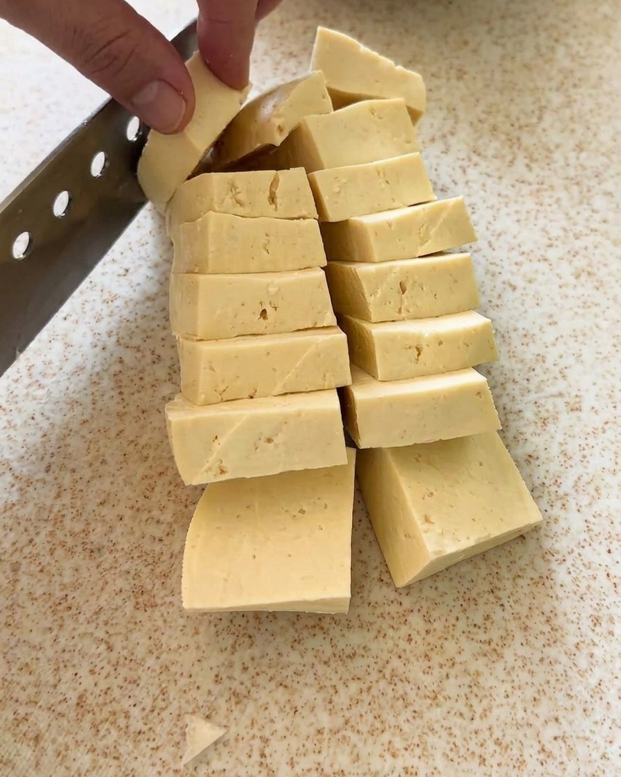Un bloc de tofu découpé en cubes réguliers sur une planche.