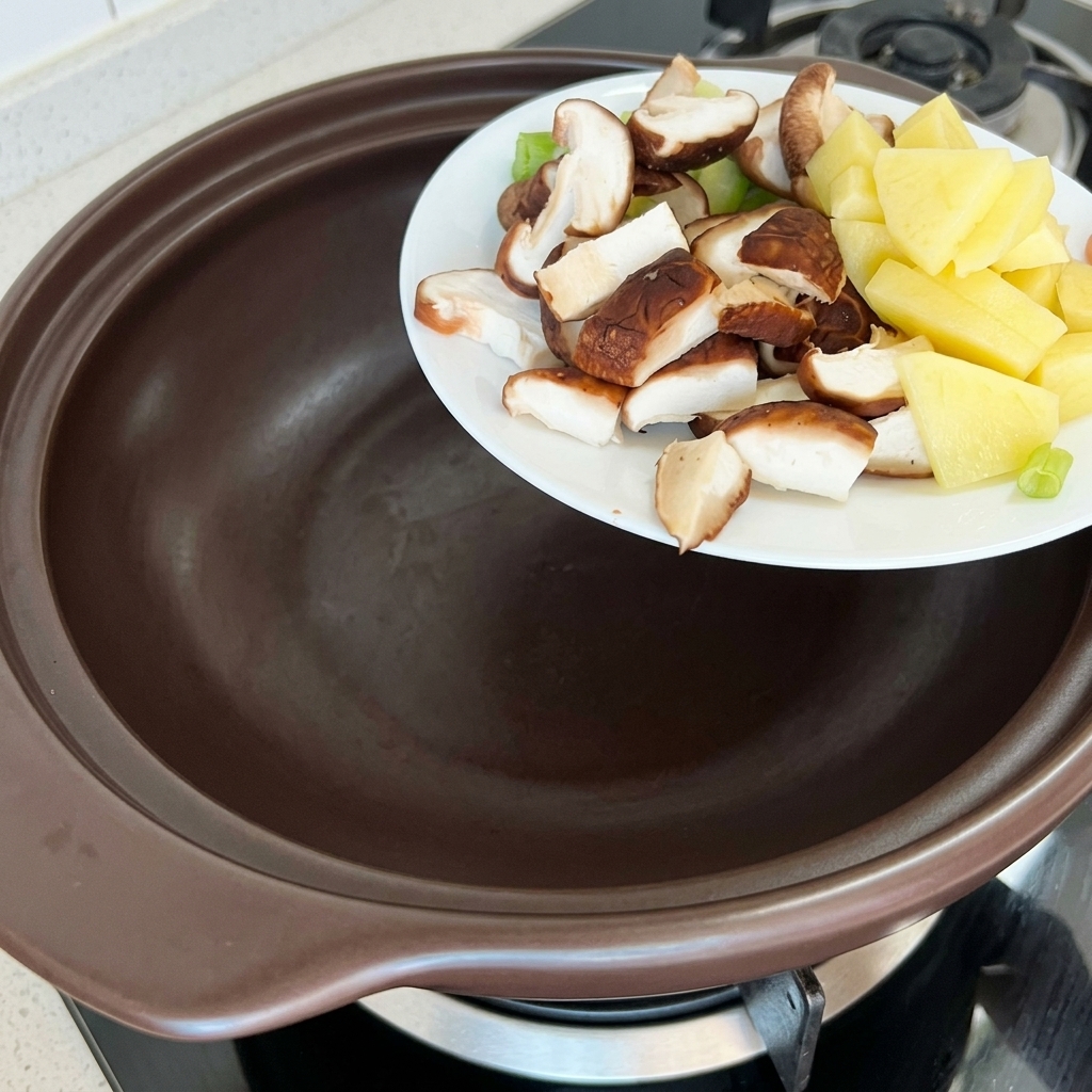 Pommes de terre, courgettes et shiitakes ajoutés dans un pot en terre cuite.