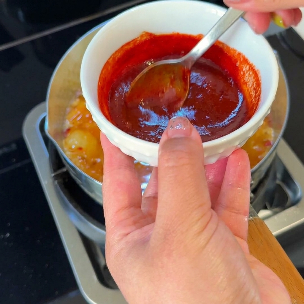 Une cuillère versant un mélange de sauce rouge vif et épicée dans le ragoût de kimchi frémissant.