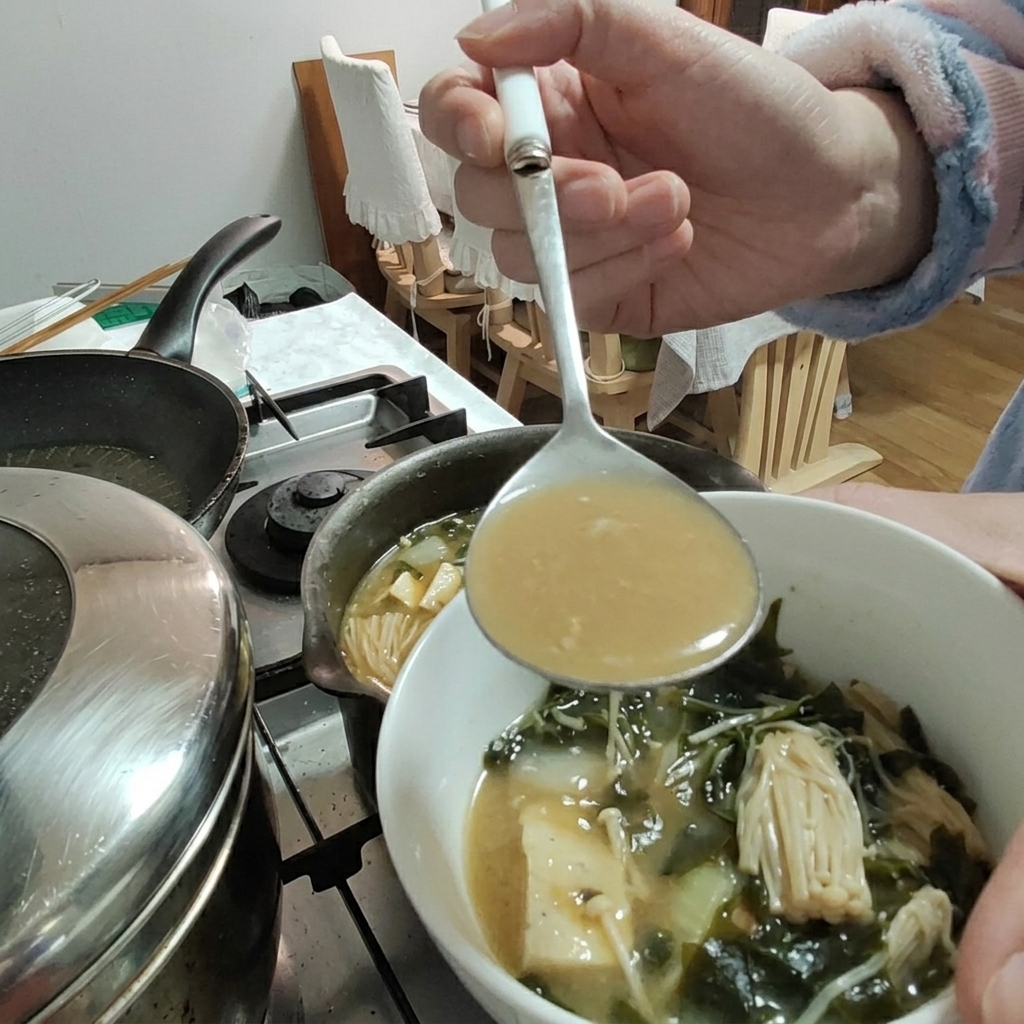 Pâte de soja ajoutée au ragoût avec une louche, tofu et champignons enoki visibles.