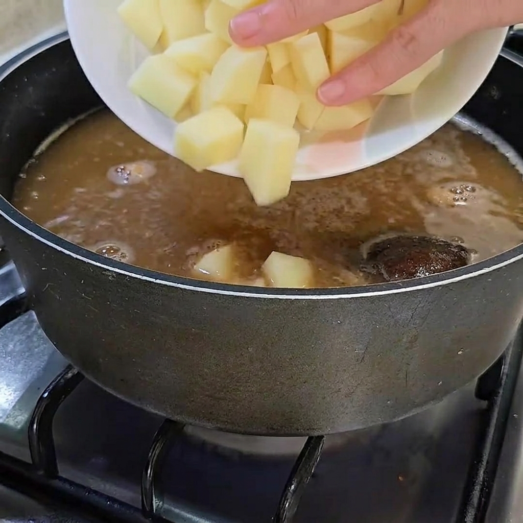 Des cubes de pommes de terre crus ajoutés dans la marmite.