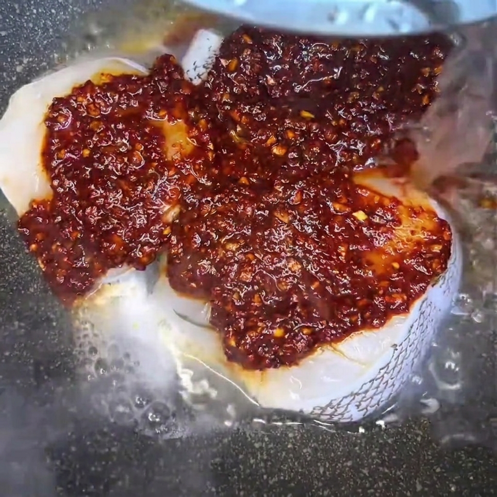 De leau versée dans la poêle sur les filets assaisonnés pour créer un bouillon de cuisson.