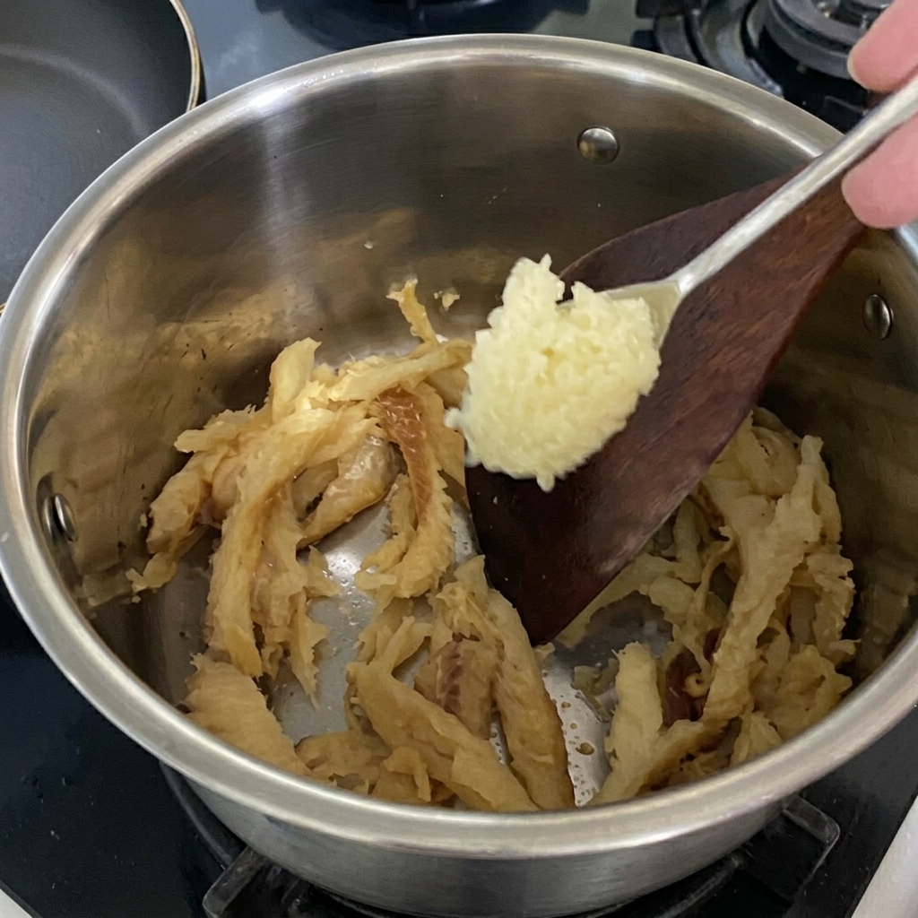 Ajout dune cuillerée dail haché dans la casserole avec le colin.