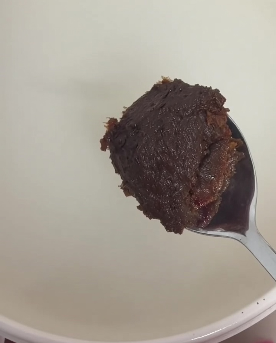 Une cuillère de pâte de soja brune et de pâte de piment rouge incorporées au bouillon.
