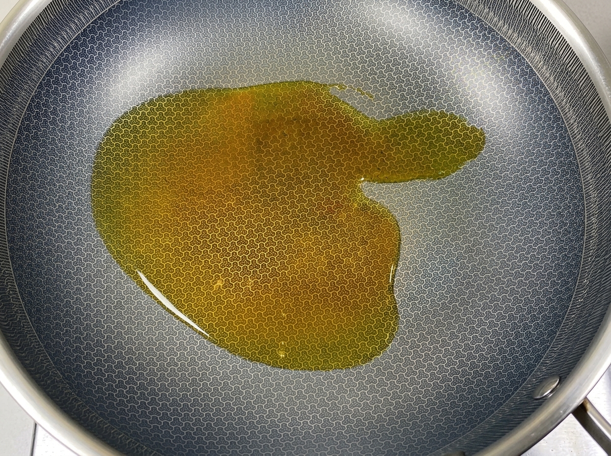 Un morceau de saindoux blanc solide fondant dans de lhuile de cuisson chaude dans un wok texturé sombre.