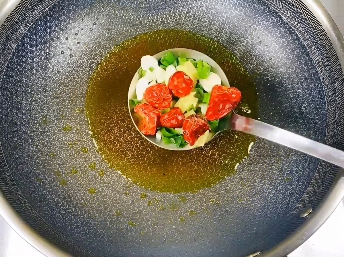Cives hachées, tranches dail et piments rouges séchés sautés dans de lhuile chaude dans une louche en métal.