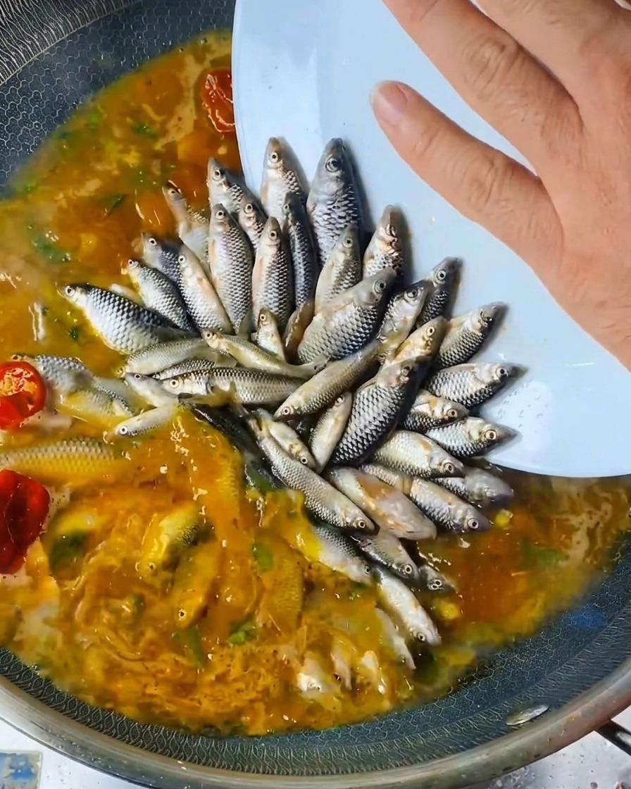 Une main versant un assaisonnement liquide depuis une bouteille sur les poissons disposés dans le wok.