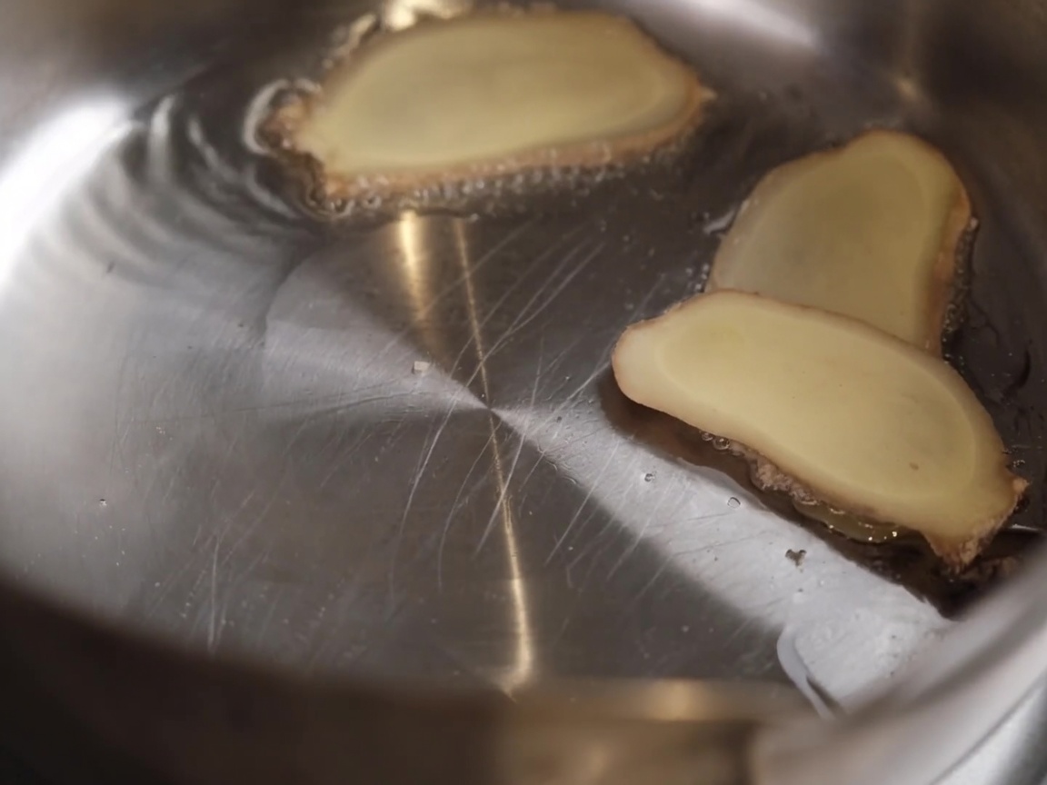 Lamelles de gingembre et ail écrasé qui cuisent dans lhuile chaude.