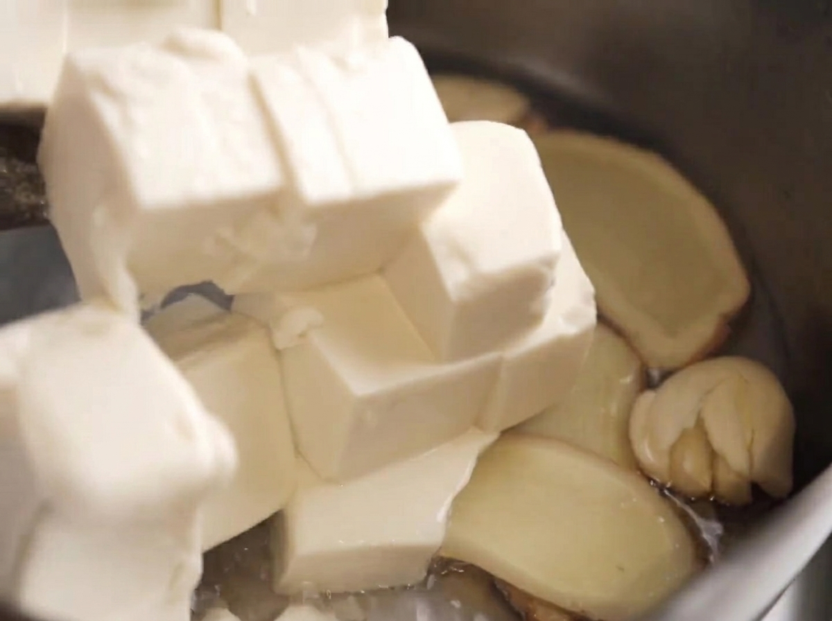 Cubes de tofu soyeux déposés délicatement dans la casserole avec les aromates.
