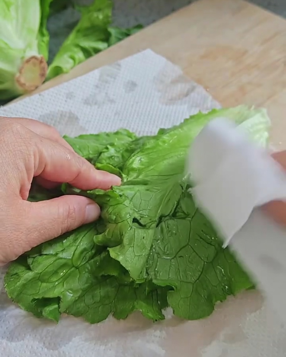 Mains séchant des feuilles de laitue fraîche sur des essuie-tout blancs posés sur une planche en bois.