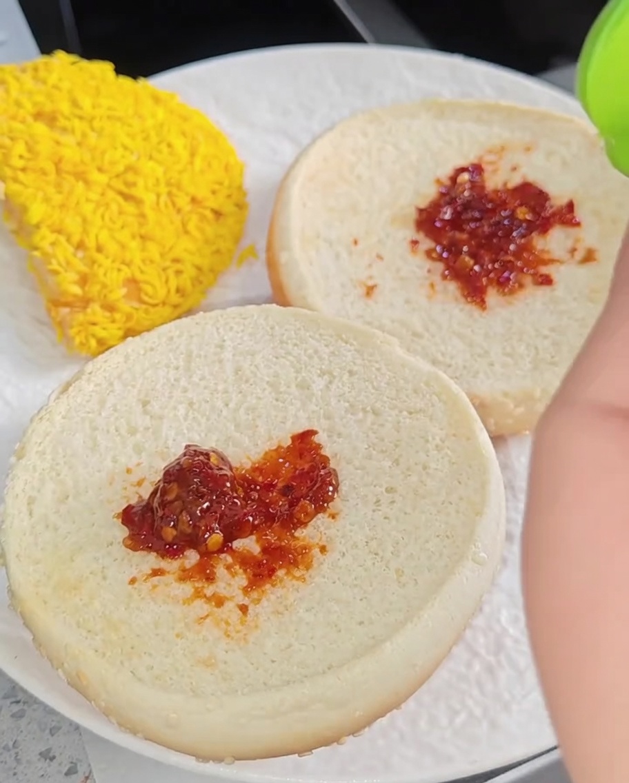 Un burger au poulet entièrement assemblé avec des couches de laitue, deux filets de poulet, du fromage et une tranche de tomate sur une assiette.