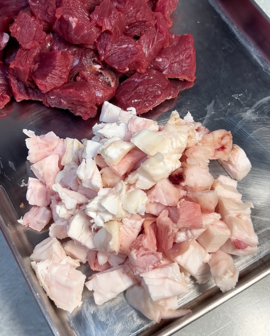 Morceaux de bœuf et de gras assaisonnés de sel et de poivre dans un bol en inox.