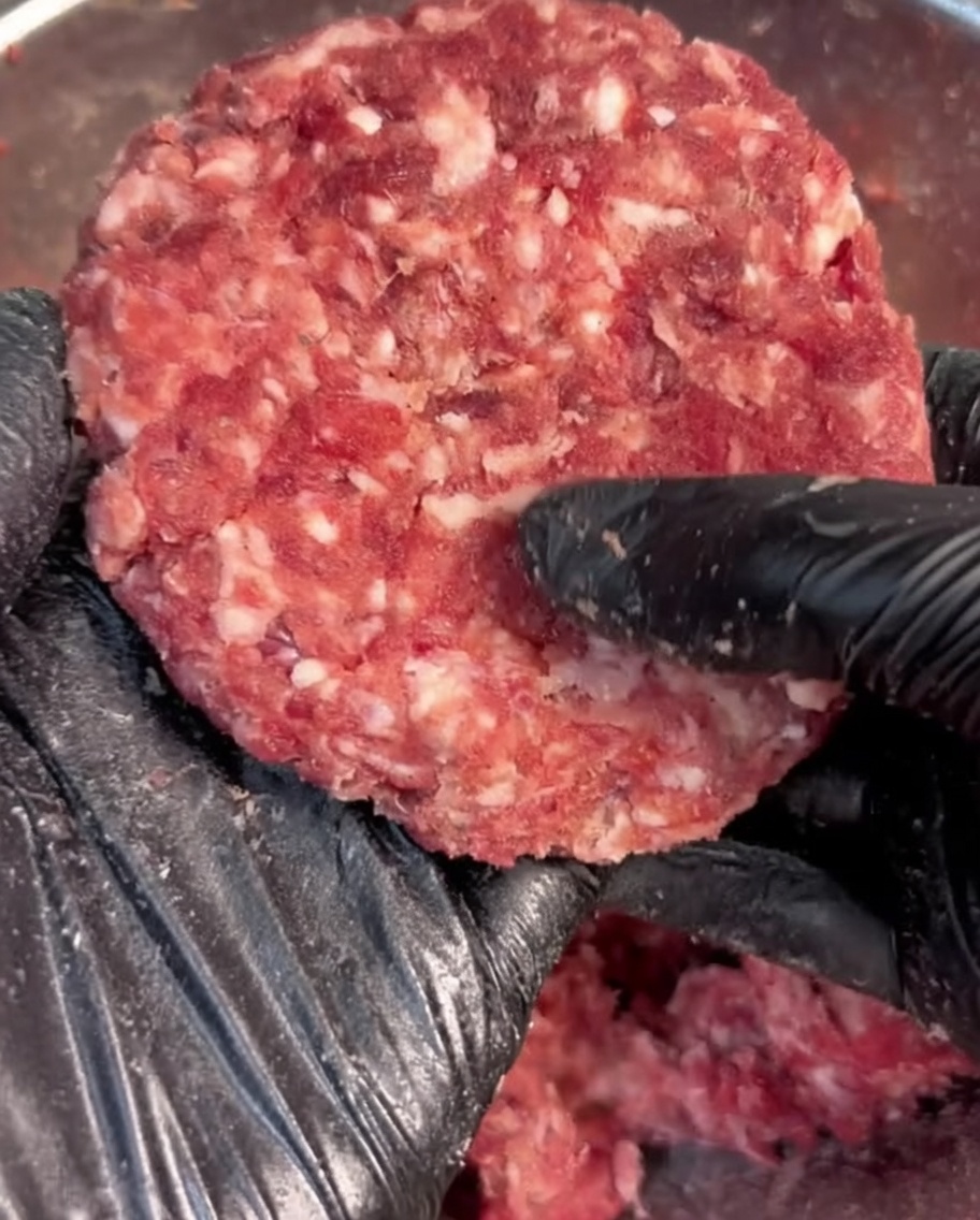 Main gantée de noir façonnant du bœuf haché assaisonné en un steak rond.