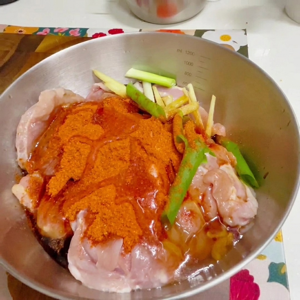 Une main gantée mélangeant le poulet assaisonné dans un bol en métal.