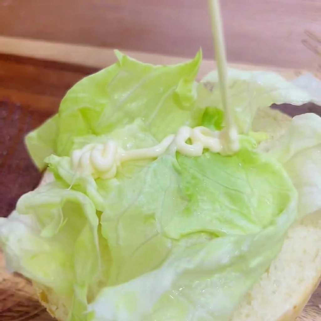 De la mayonnaise blanche appliquée en zig-zag sur la laitue fraîche dans le pain à burger.