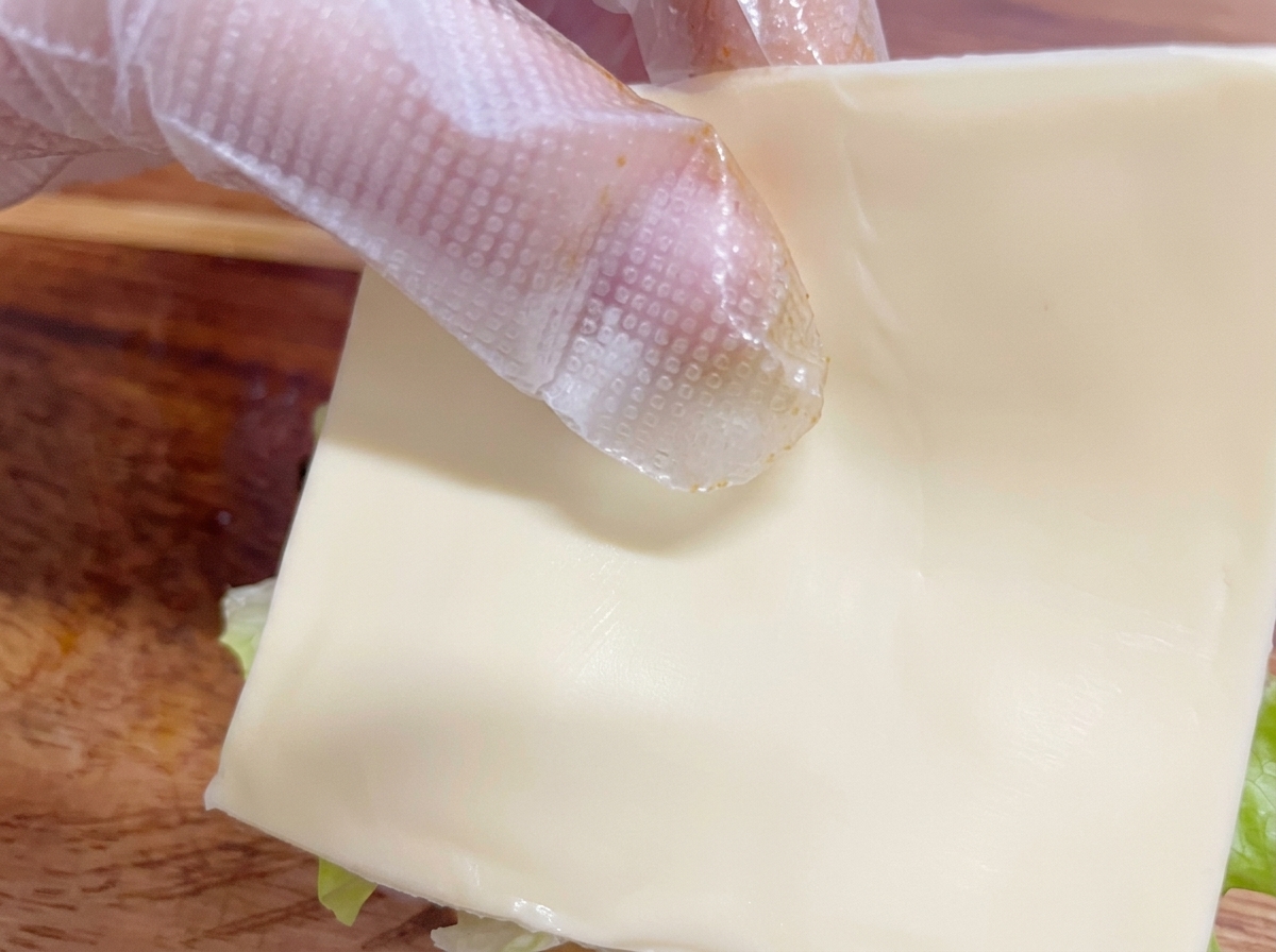 Une main gantée plaçant une tranche de fromage blanc sur le poulet.