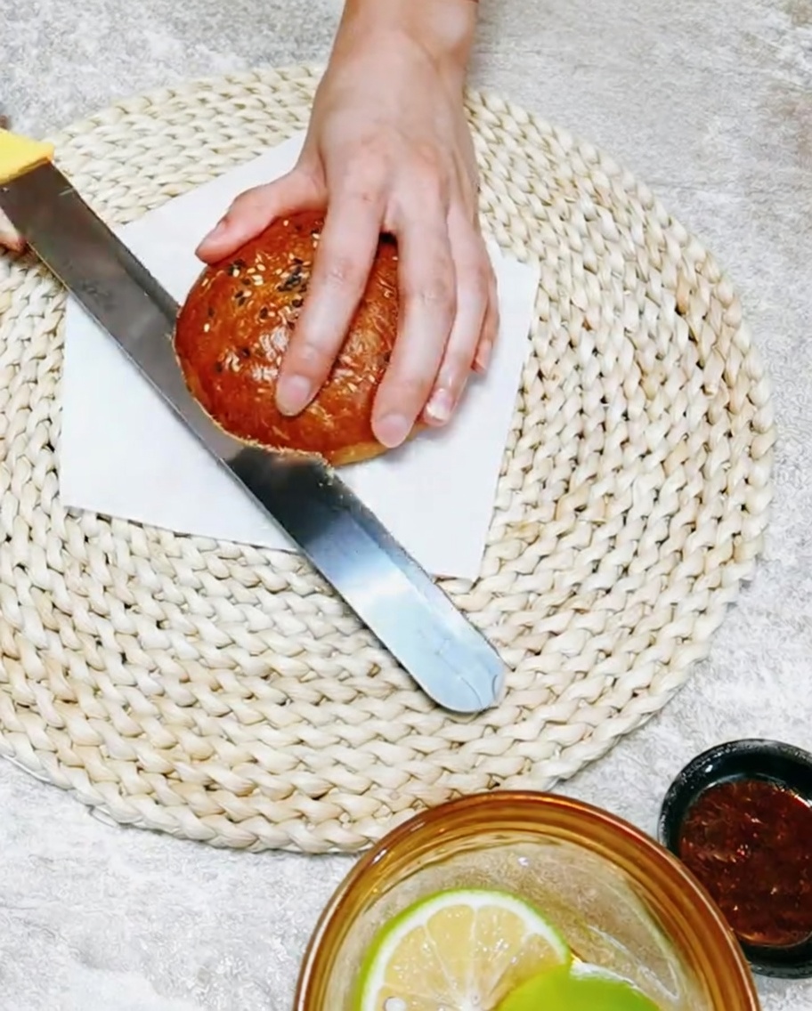 Une main utilisant un couteau pour trancher un pain à burger fait maison sur une planche à découper.