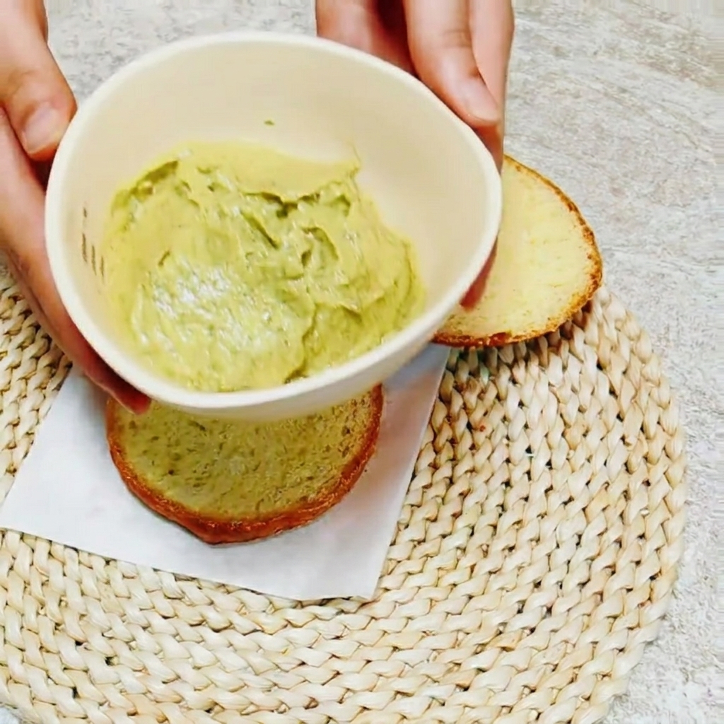 Gros plan sur une lame de couteau étalant de la sauce verte avocat-basilic sur lintérieur dun pain à burger.