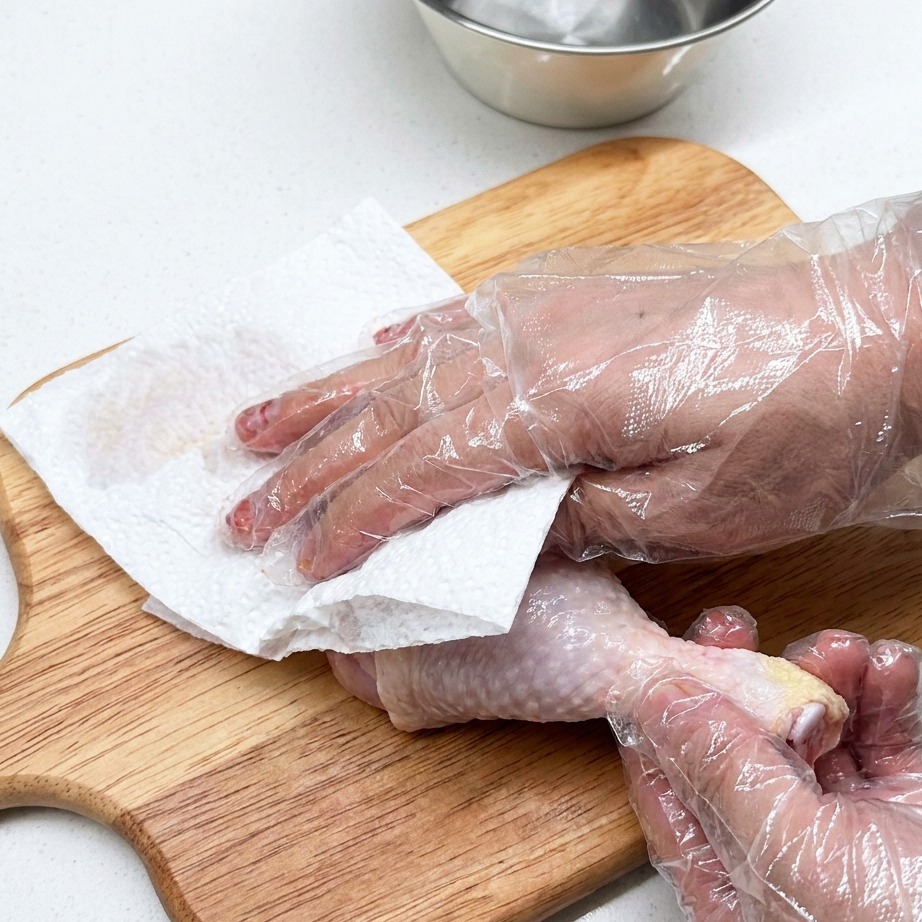 Une cuisse de poulet crue en cours de préparation sur une planche à découper en bois avec du papier absorbant.
