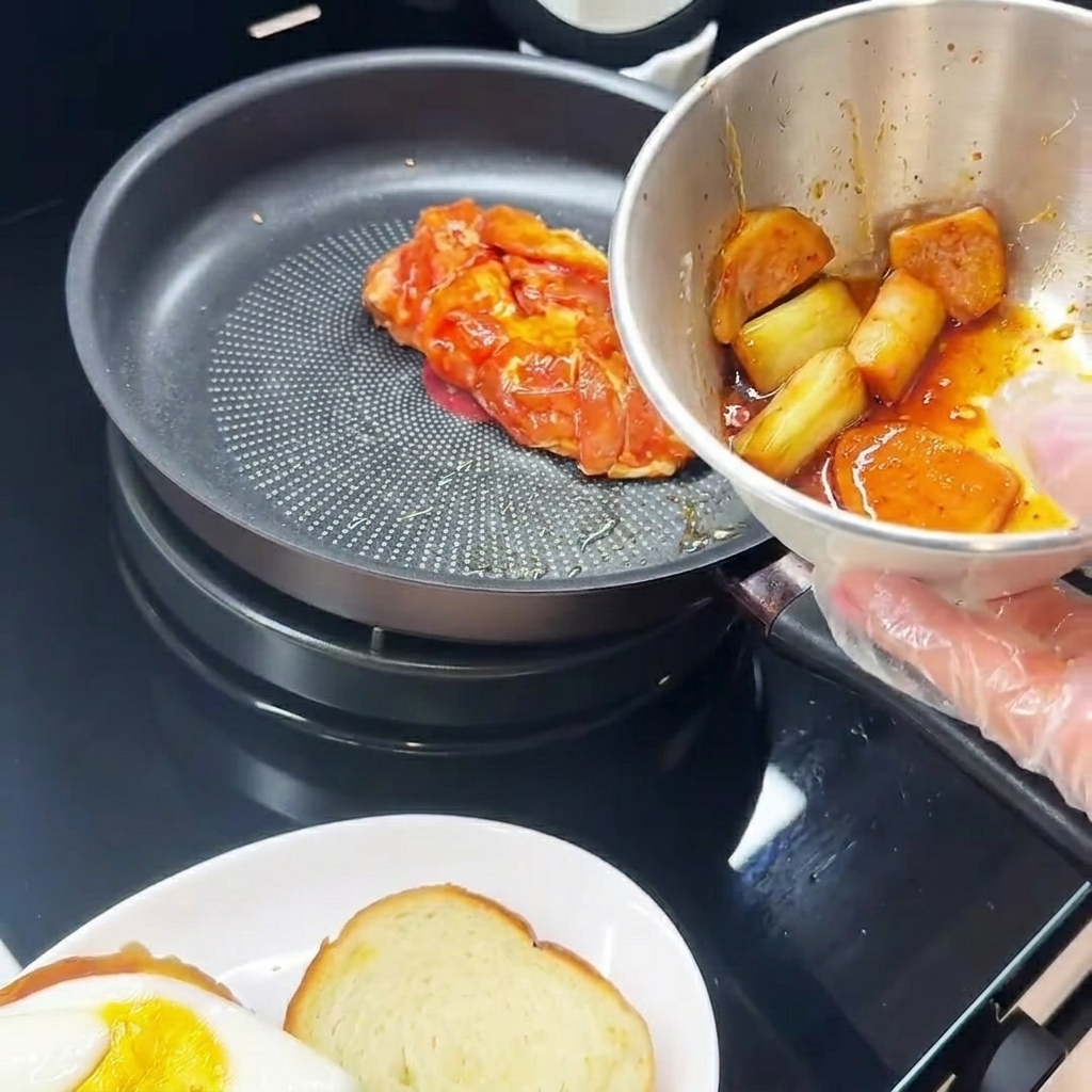 Haut de cuisse de poulet mariné cuisant côté peau dans une poêle, à côté dune assiette avec un œuf au plat.