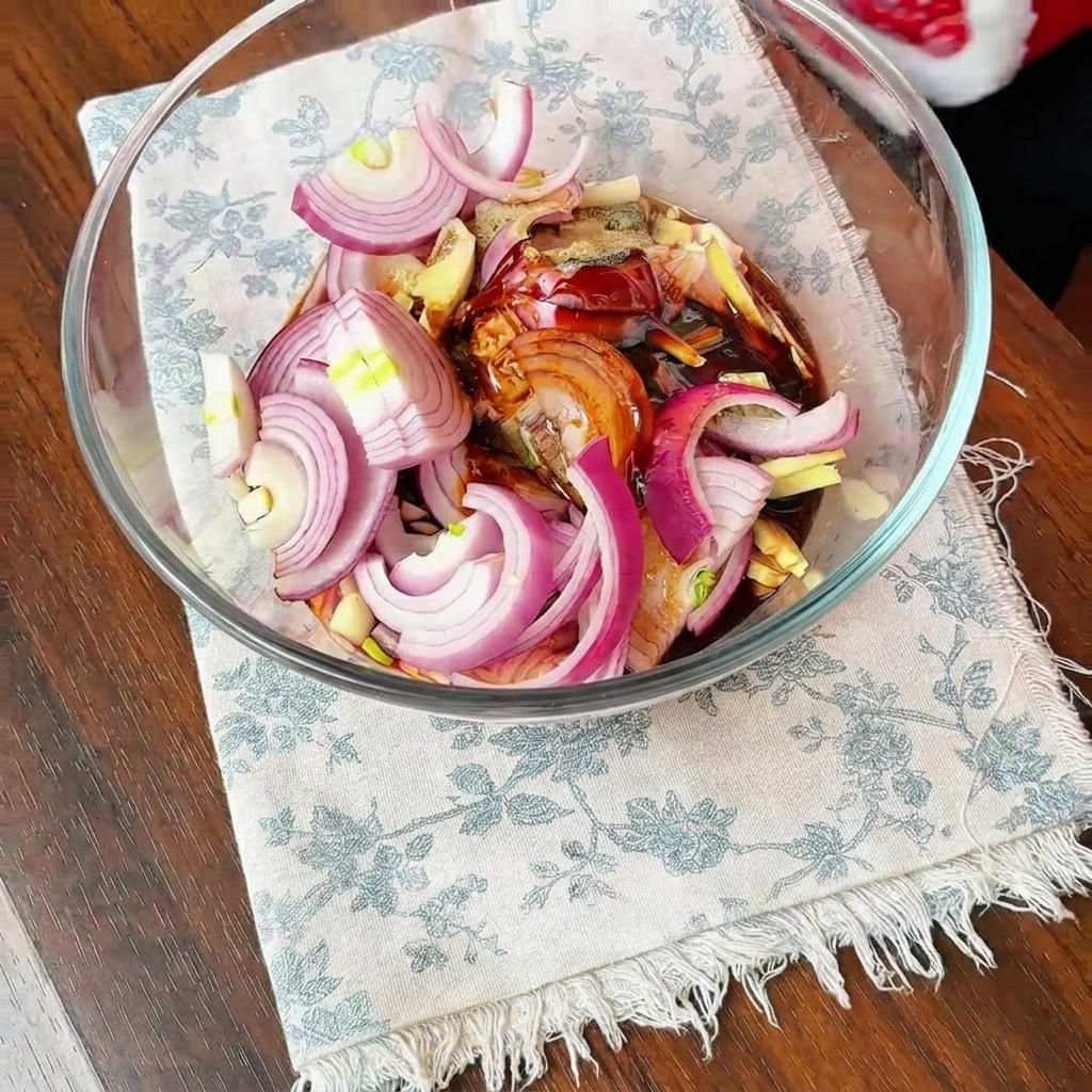 Hauts de cuisses de poulet, oignons émincés et assaisonnements pour marinade foncée mélangés dans un grand bol en verre.
