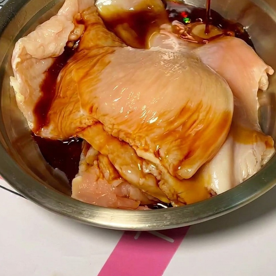 Tranches de poulet cru dans un bol, enrobées dune marinade sombre et savoureuse.