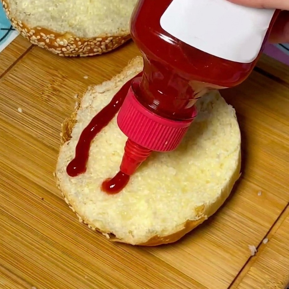 Un filet de ketchup rouge appliqué au centre dun pain à burger aux graines de sésame grillé.