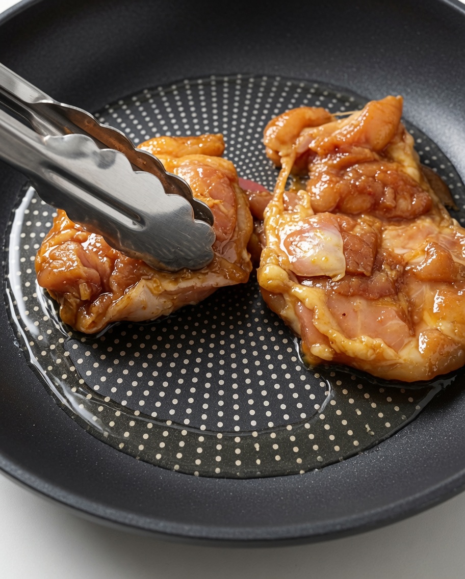 Cuisses de poulet marinées crues déposées dans une poêle chaude huilée avec des pinces de cuisine.