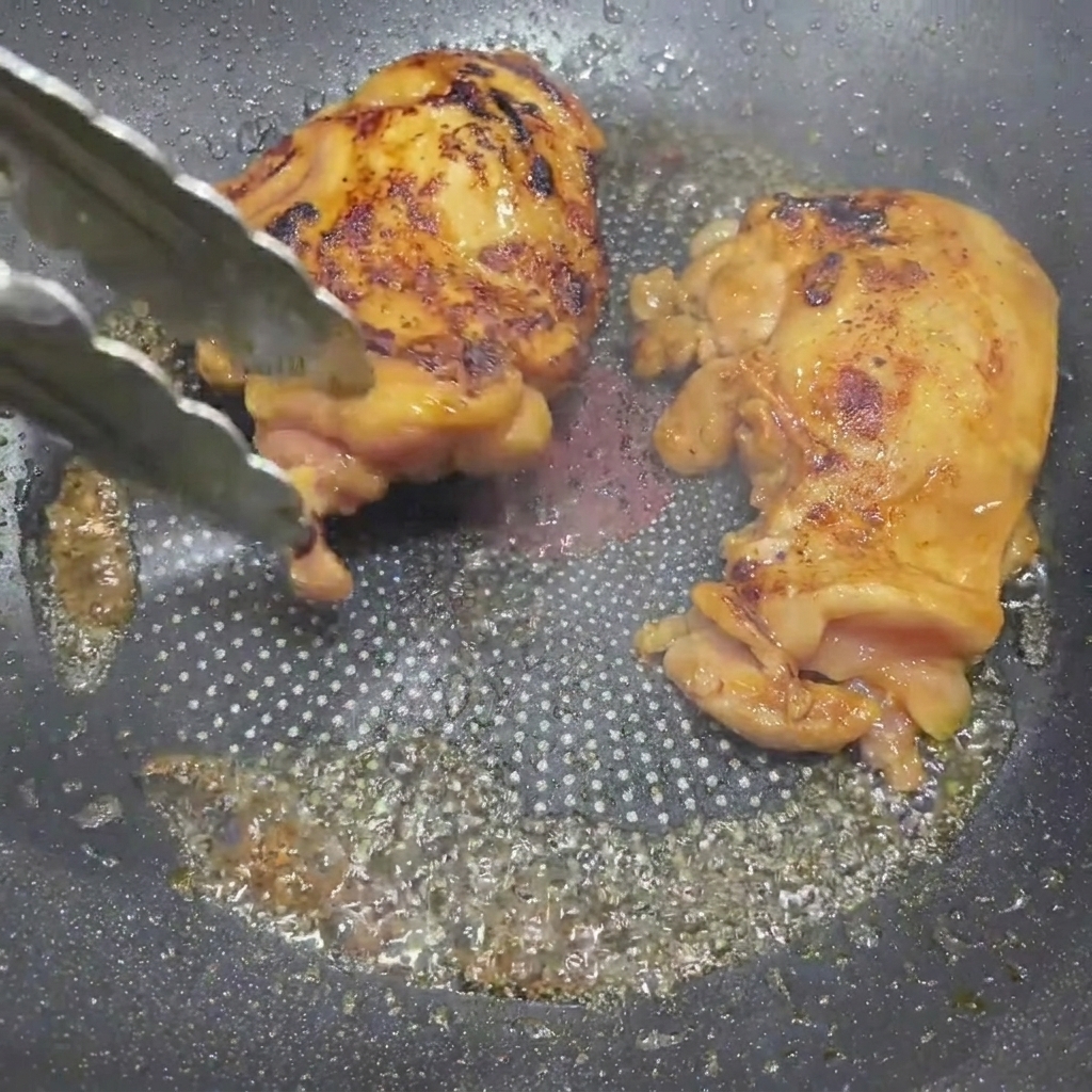 Cuisses de poulet laquées au teriyaki dorées retournées dans une poêle avec des pinces.