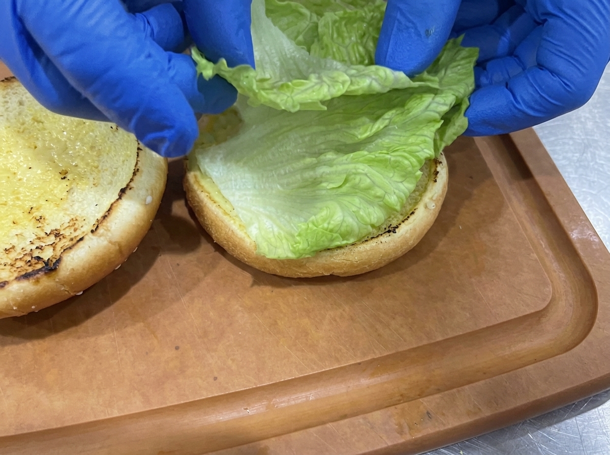Feuilles de laitue verte croquante disposées sur la base du pain à burger toasté.