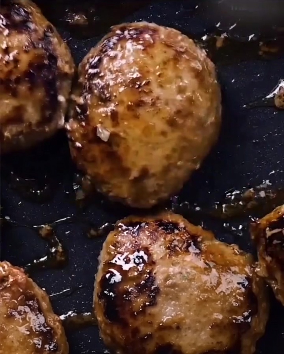 Des steaks hachés luisants dun glaçage teriyaki sombre et épais dans une poêle.