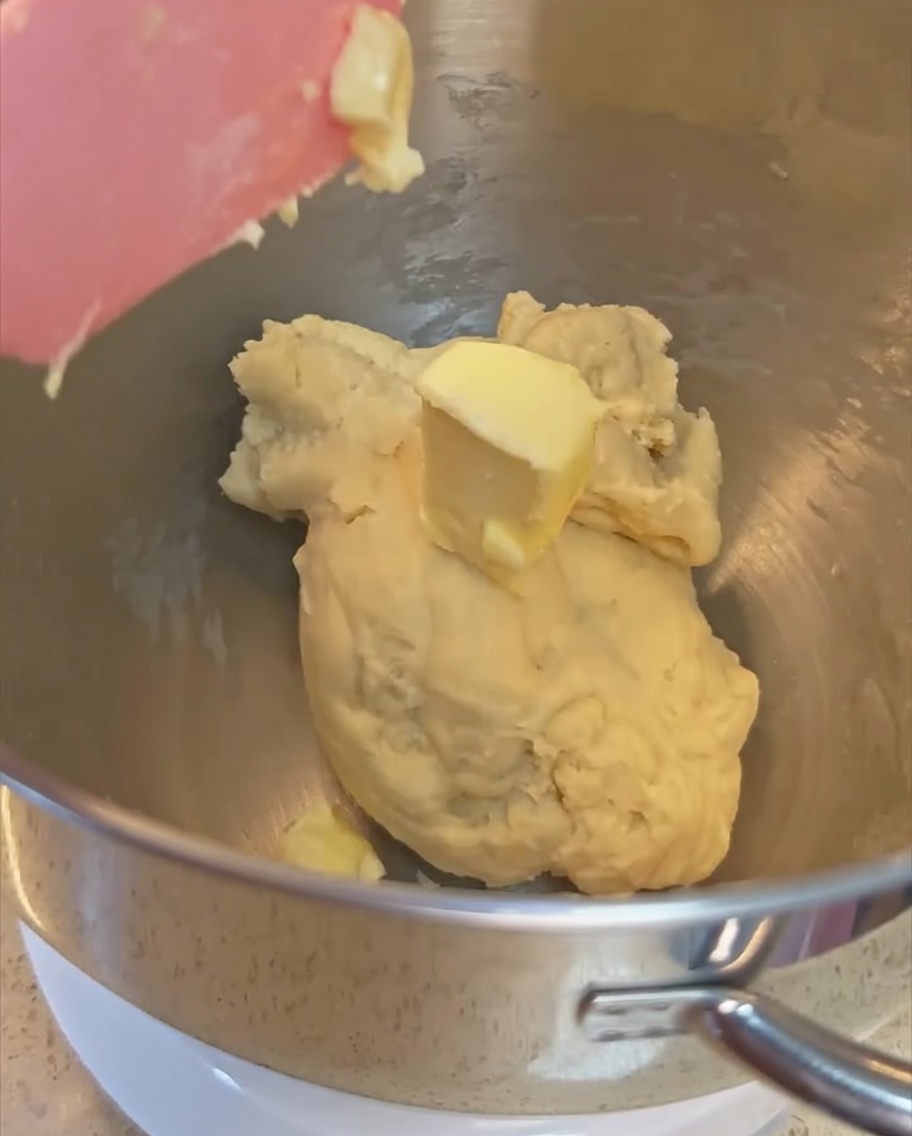 Une noisette de beurre ajoutée à la pâte partiellement pétrie dans le bol en acier inoxydable.