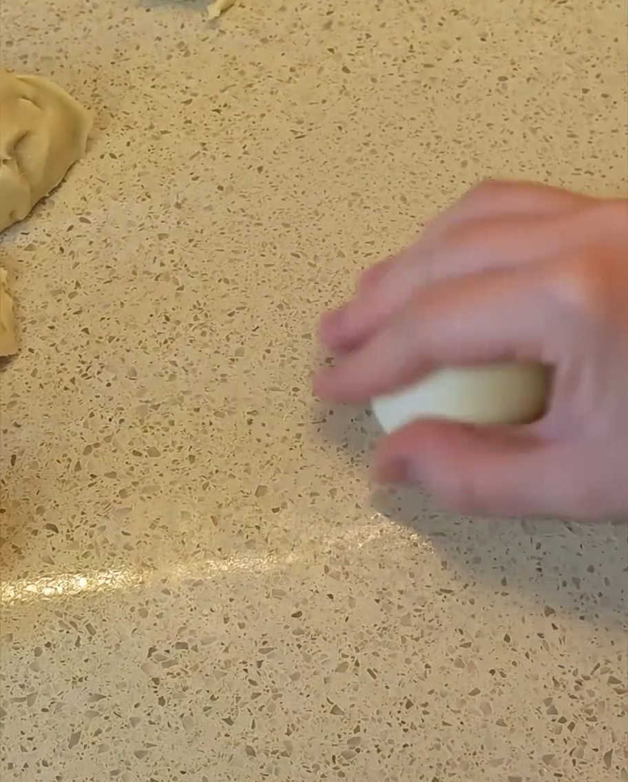 Une main roulant un morceau de pâte sur le plan de travail pour former une boule lisse.