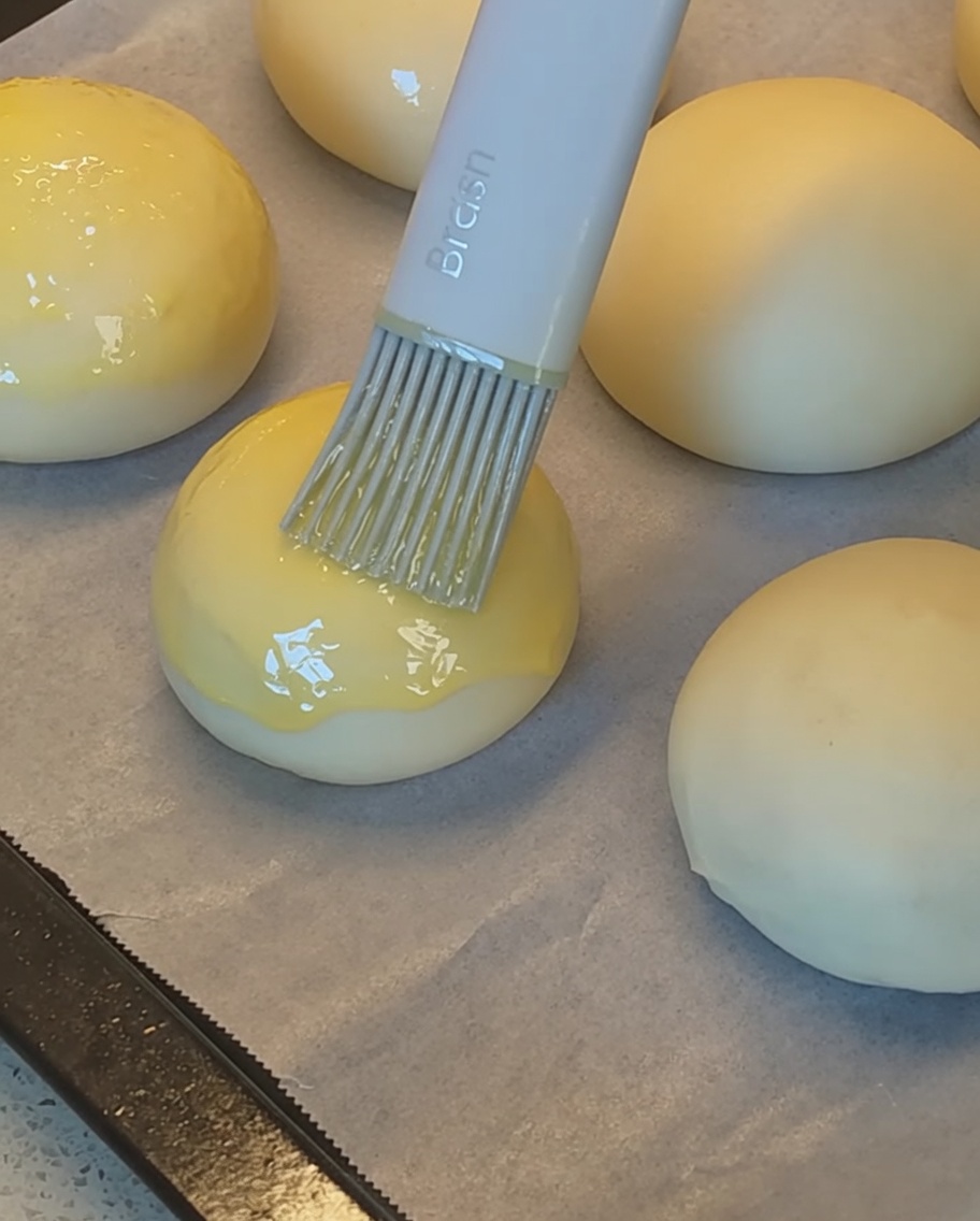 Un pinceau en silicone appliquant de la dorure sur les pains avant de les saupoudrer de graines de sésame.