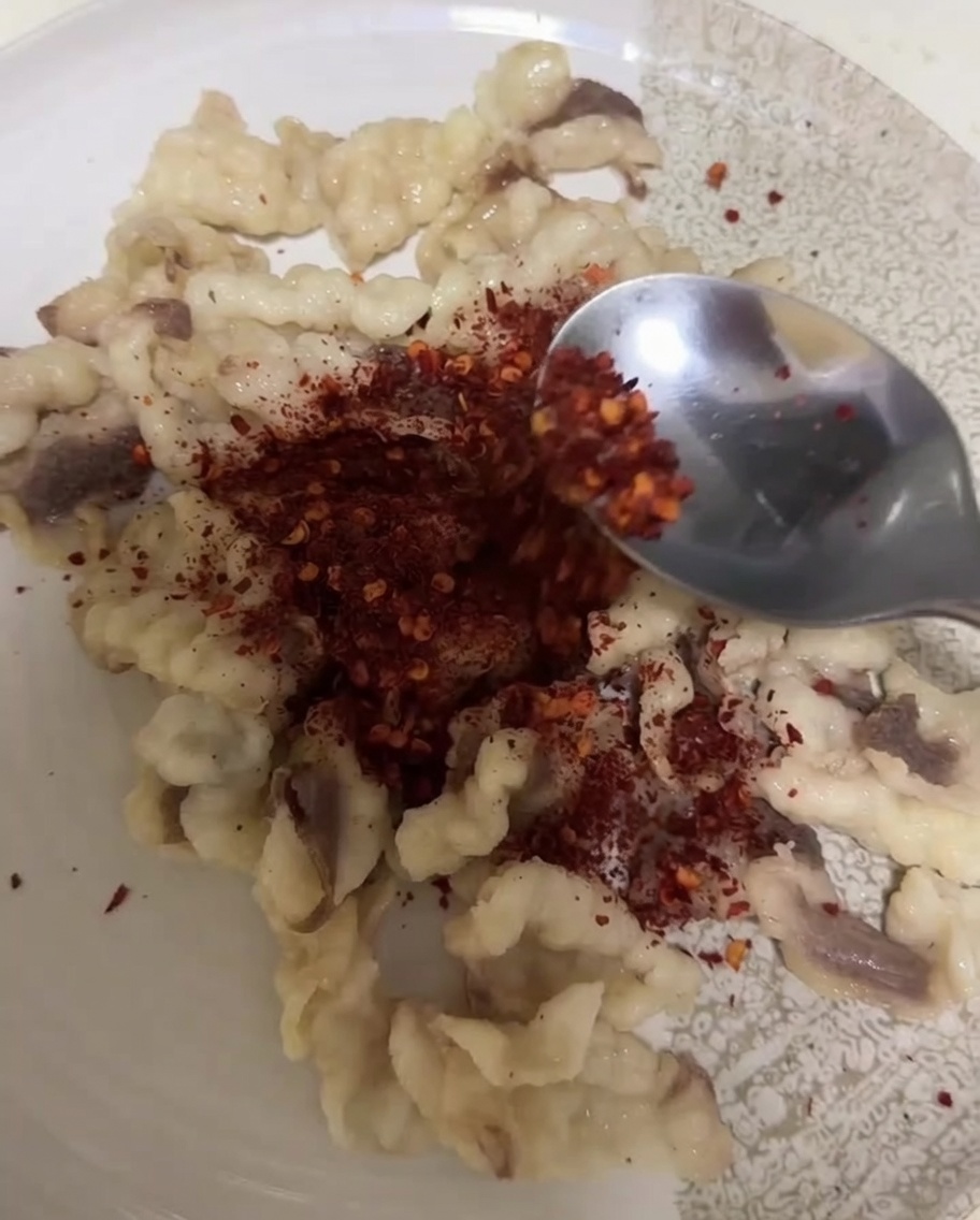 Une cuillère versant de la poudre de chili et du cumin sur des morceaux de graisse blanche blanchie.