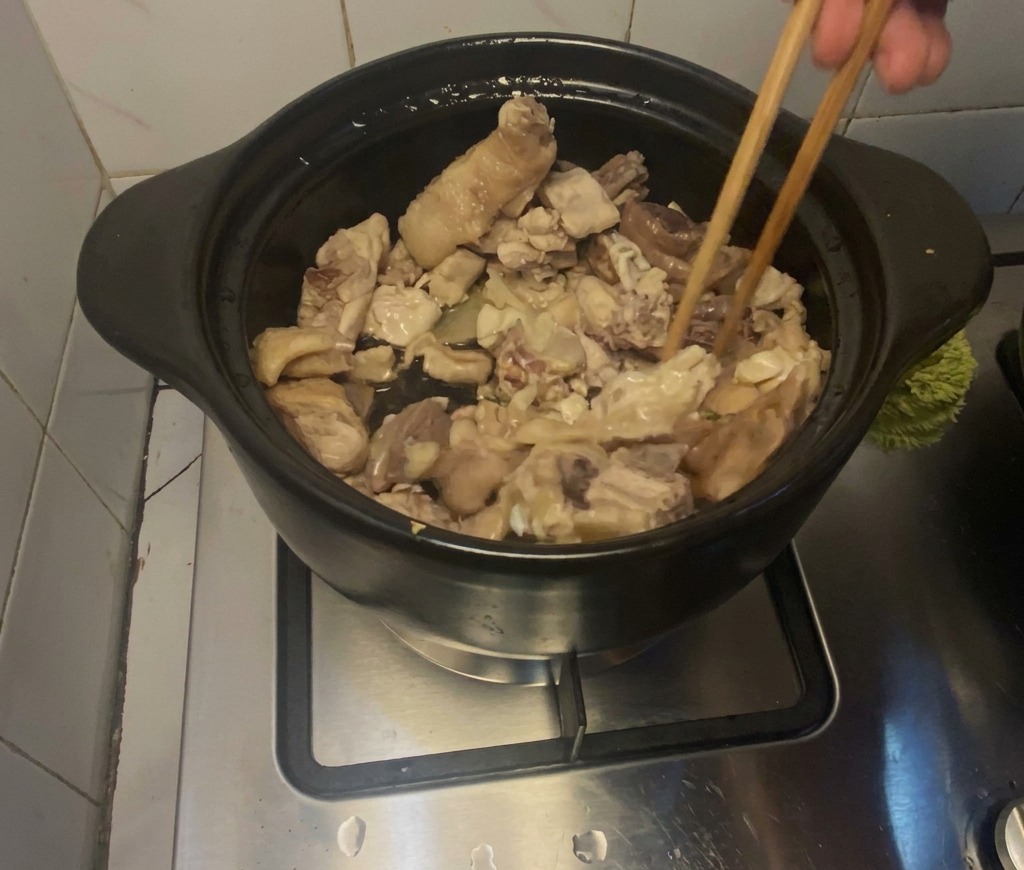 Morceaux de poulet sautés avec des baguettes dans un pot en terre cuite noir.