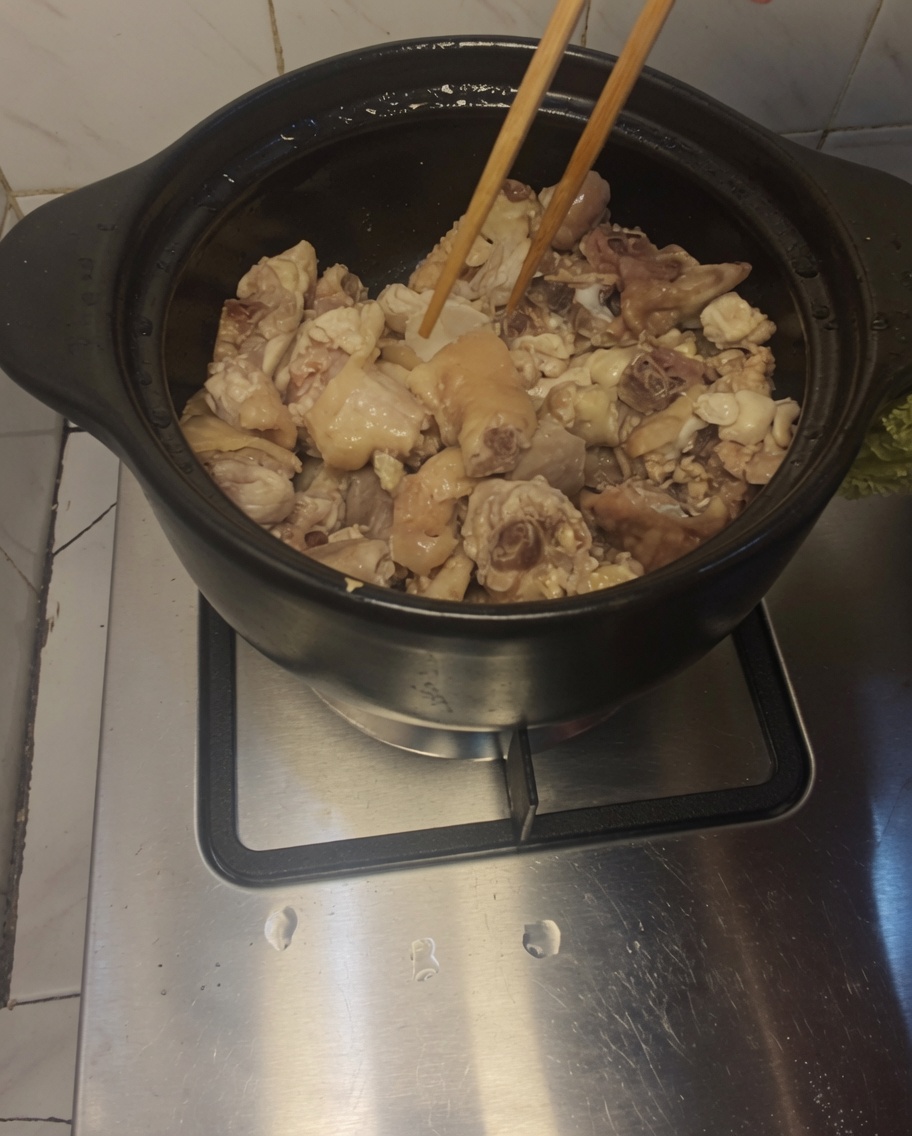 Baguettes mélangeant le poulet et les tranches de gingembre dans le pot.