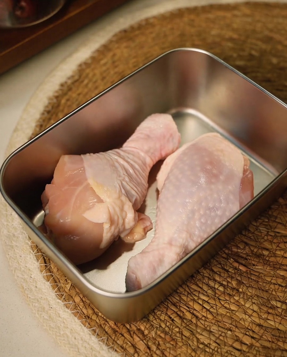 Cuisses de poulet crues taillées aux ciseaux de cuisine dans un récipient en métal.