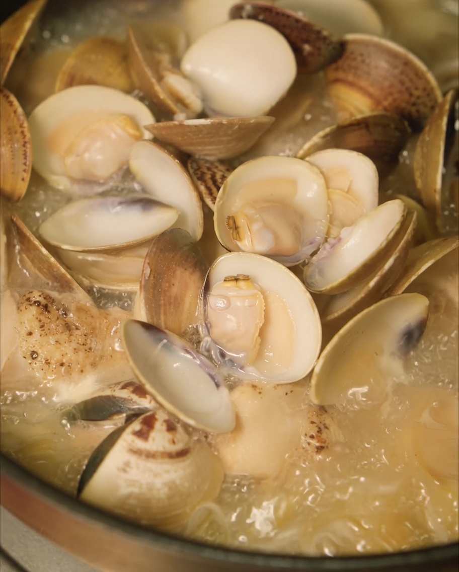 Palourdes fraîches ajoutées à la poêle de poulet et doignons pour cuire à la vapeur.