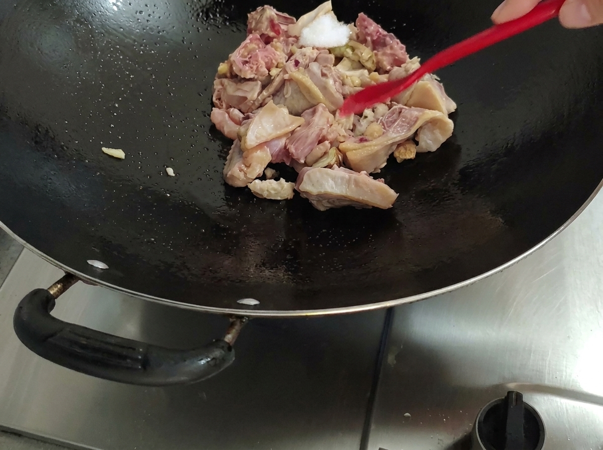 Ajout de sel sur le poulet dans le wok avec une spatule rouge.