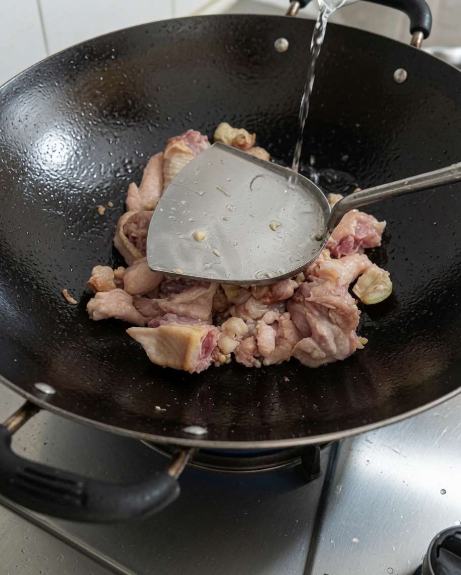 Verser de leau fraîche dans le wok contenant le poulet saisi.