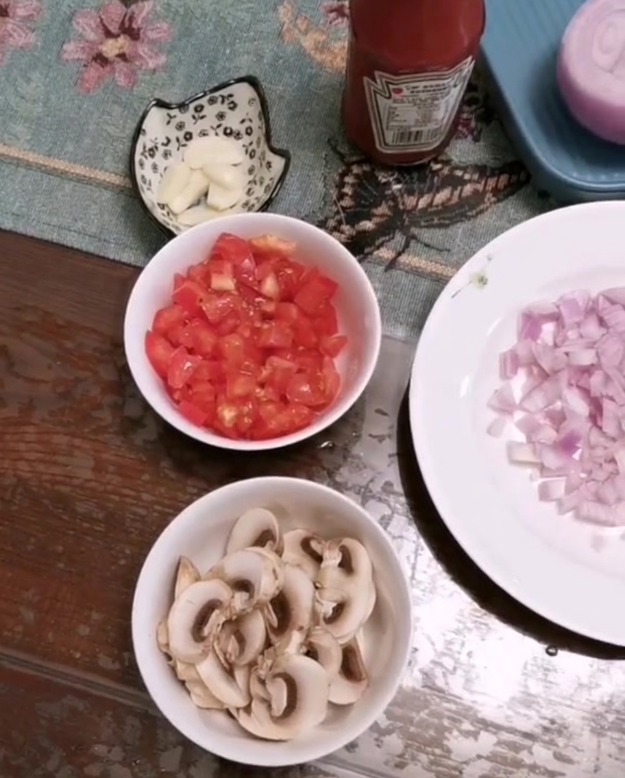 Un bol contenant des tomates fraîchement coupées, des champignons émincés et de lail haché sur une table.