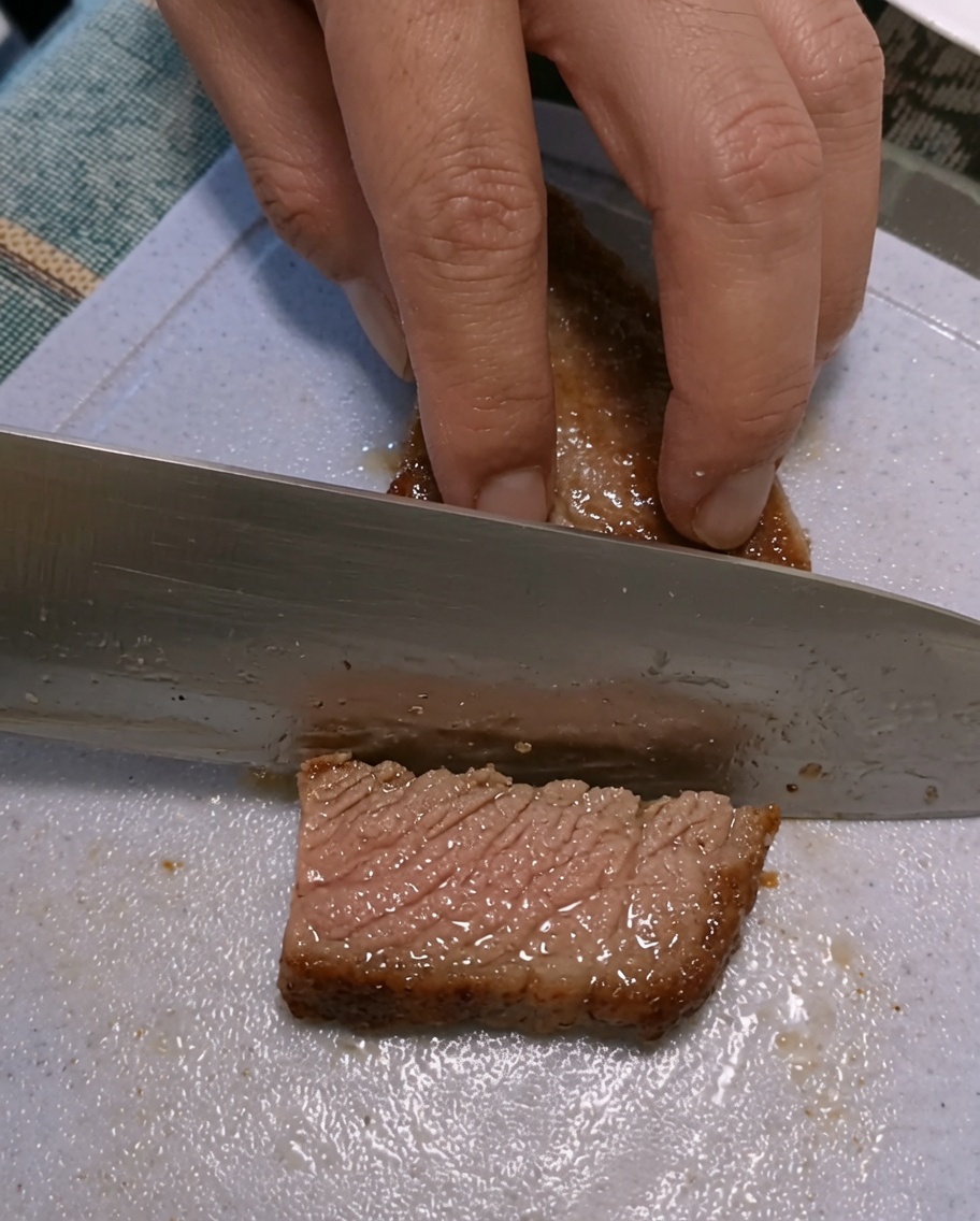 Mains tranchant un steak saisi sur une planche à découper en plastique.