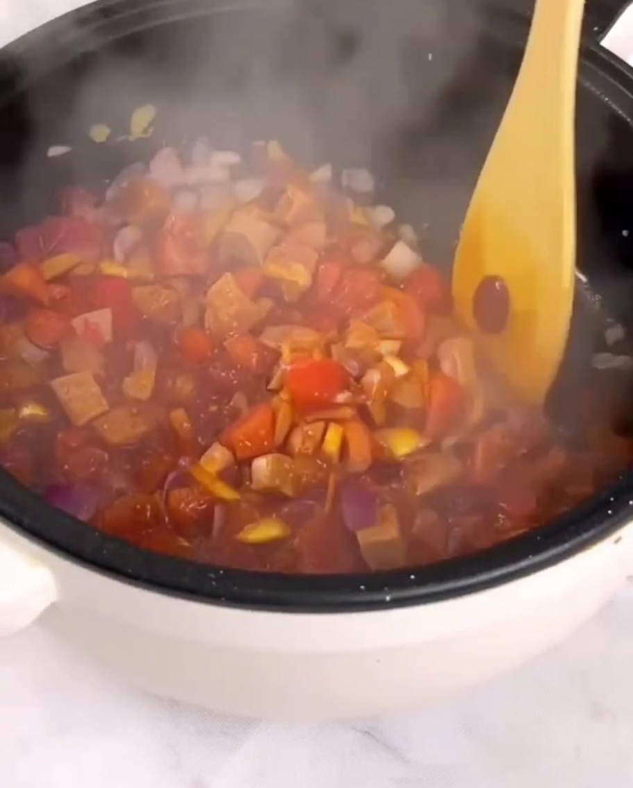Dés de tomates, jambon et légumes revenus dans une poêle avec une spatule en bois.