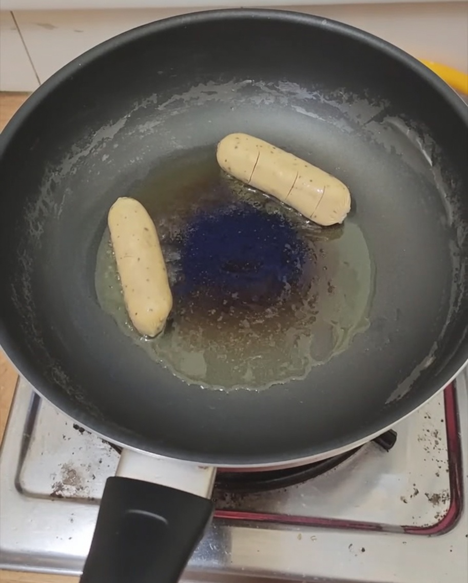 Un œuf et une saucisse en train de cuire dans une poêle.