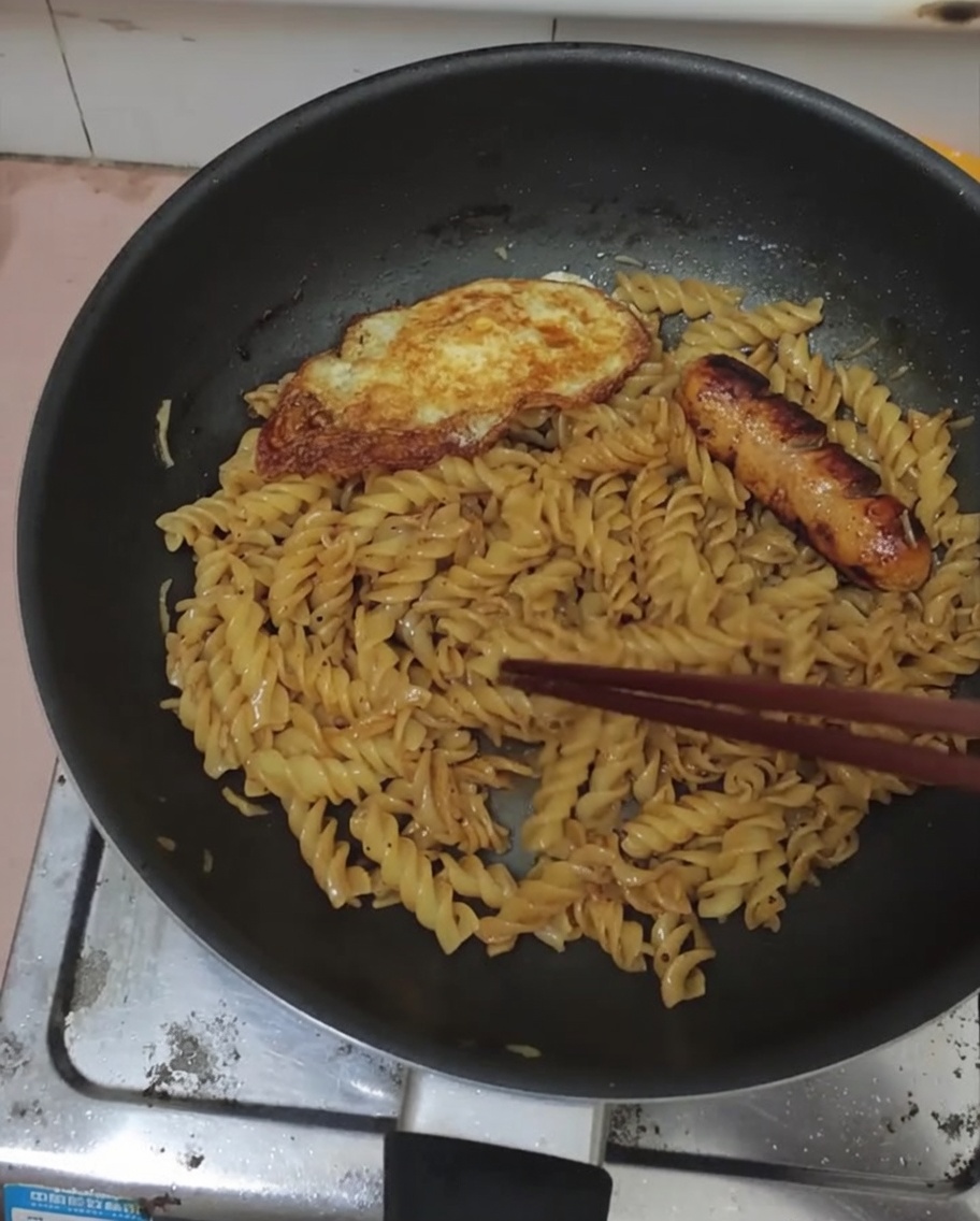 Œuf au plat et saucisse servis sur un lit de fusillis au poivre noir.