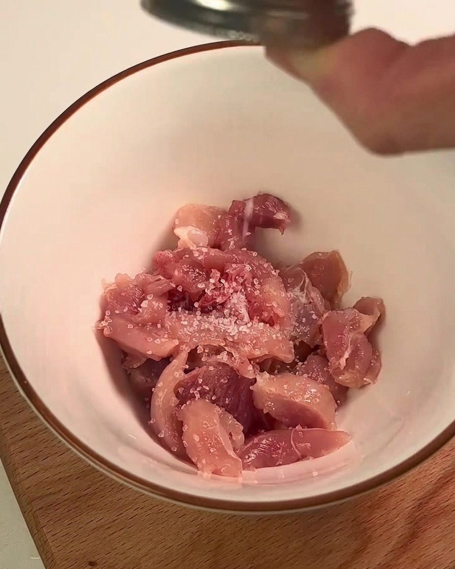 Chair de cuisse de poulet assaisonnée de sel et de jus de citron dans un bol blanc.
