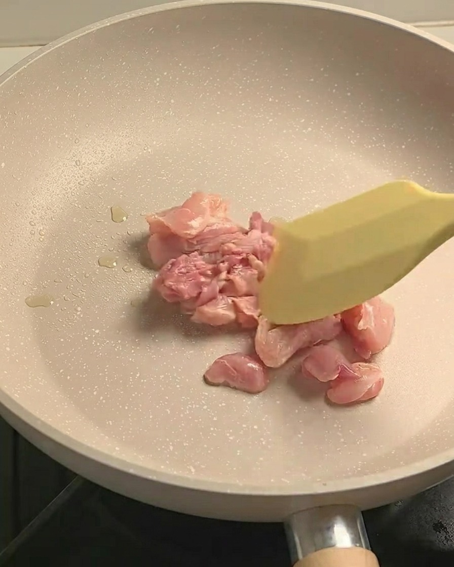 Morceaux de cuisse de poulet assaisonnés en train de sauter dans une poêle antiadhésive, montrant un léger brunissement.